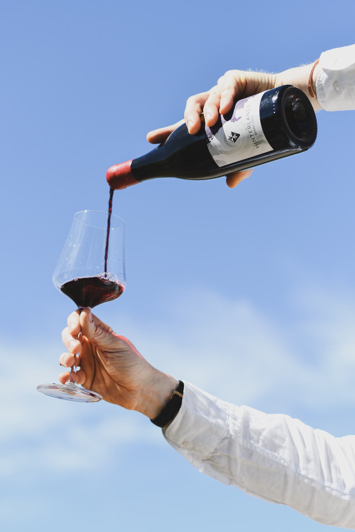 Pouring Bosman Hinterlands Syrah into a glass held up against a blue sky